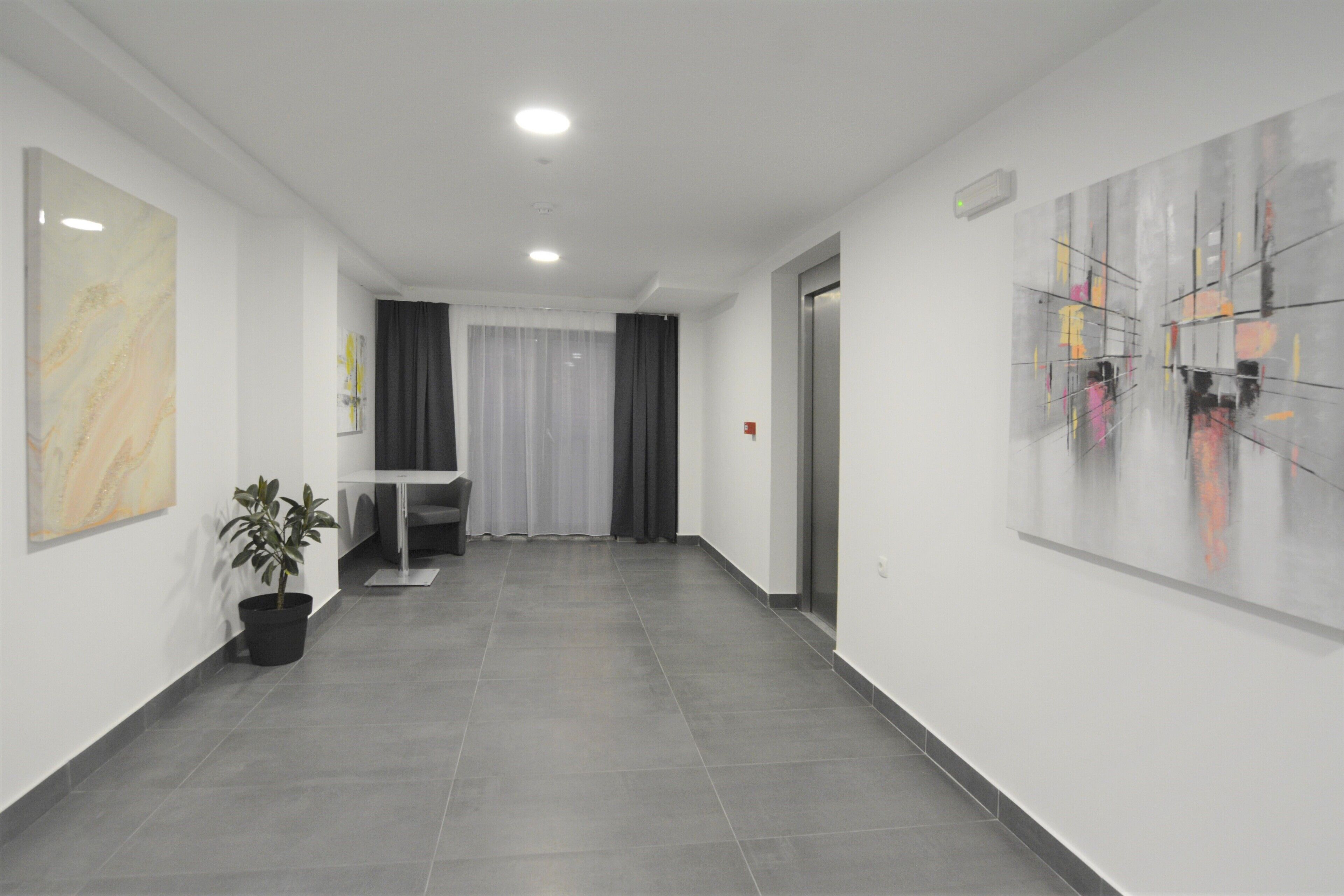 Un pasillo moderno de hotel con mostrador de recepción, una planta en maceta y arte abstracto en la pared.
