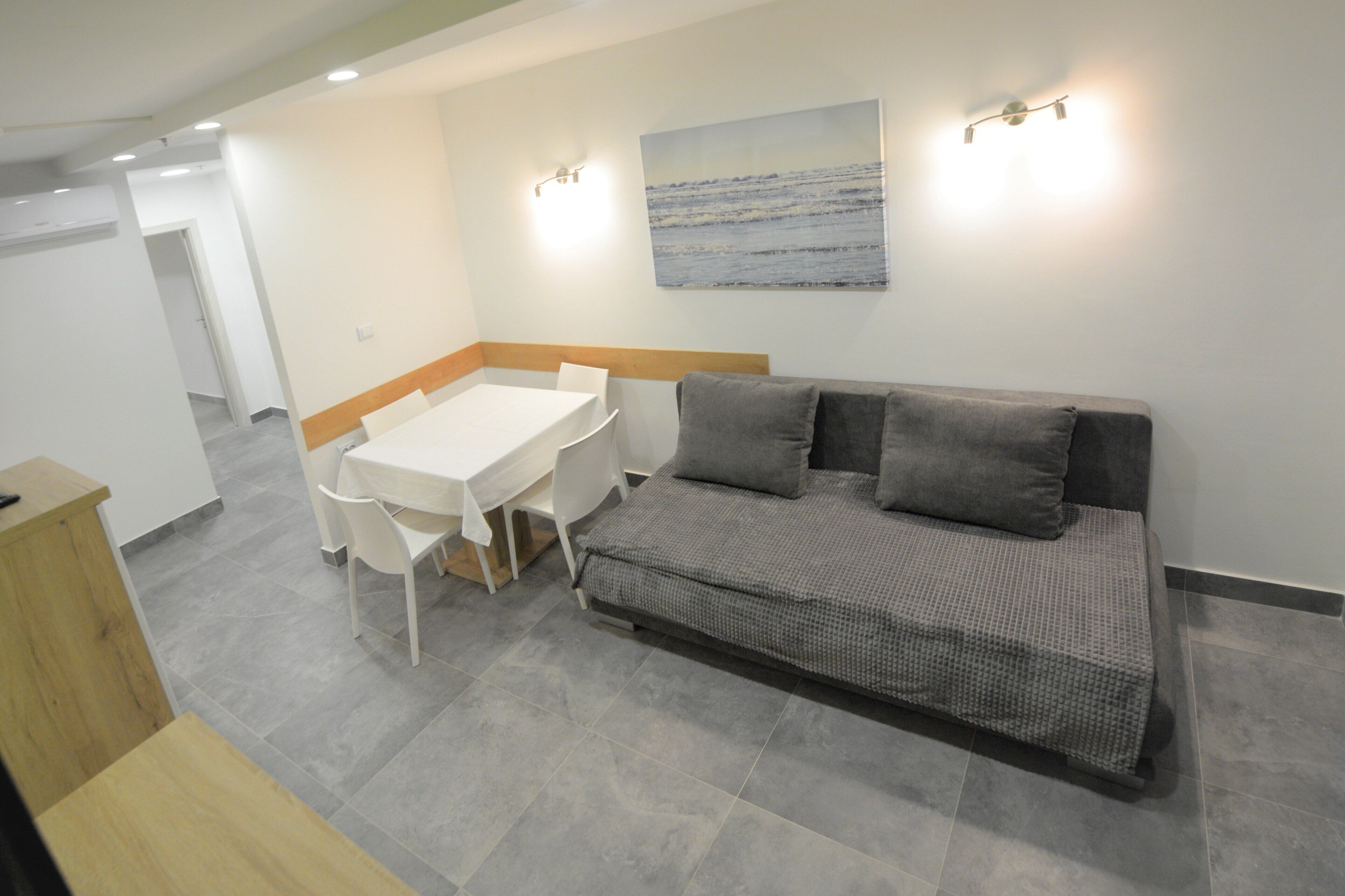 A small, modern room with a grey sofa, a white table, and a painting on the wall.