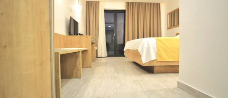Ein Hotelzimmer mit Bett, Schreibtisch, Fernseher und einer Schiebetür, die auf einen Balkon führt.