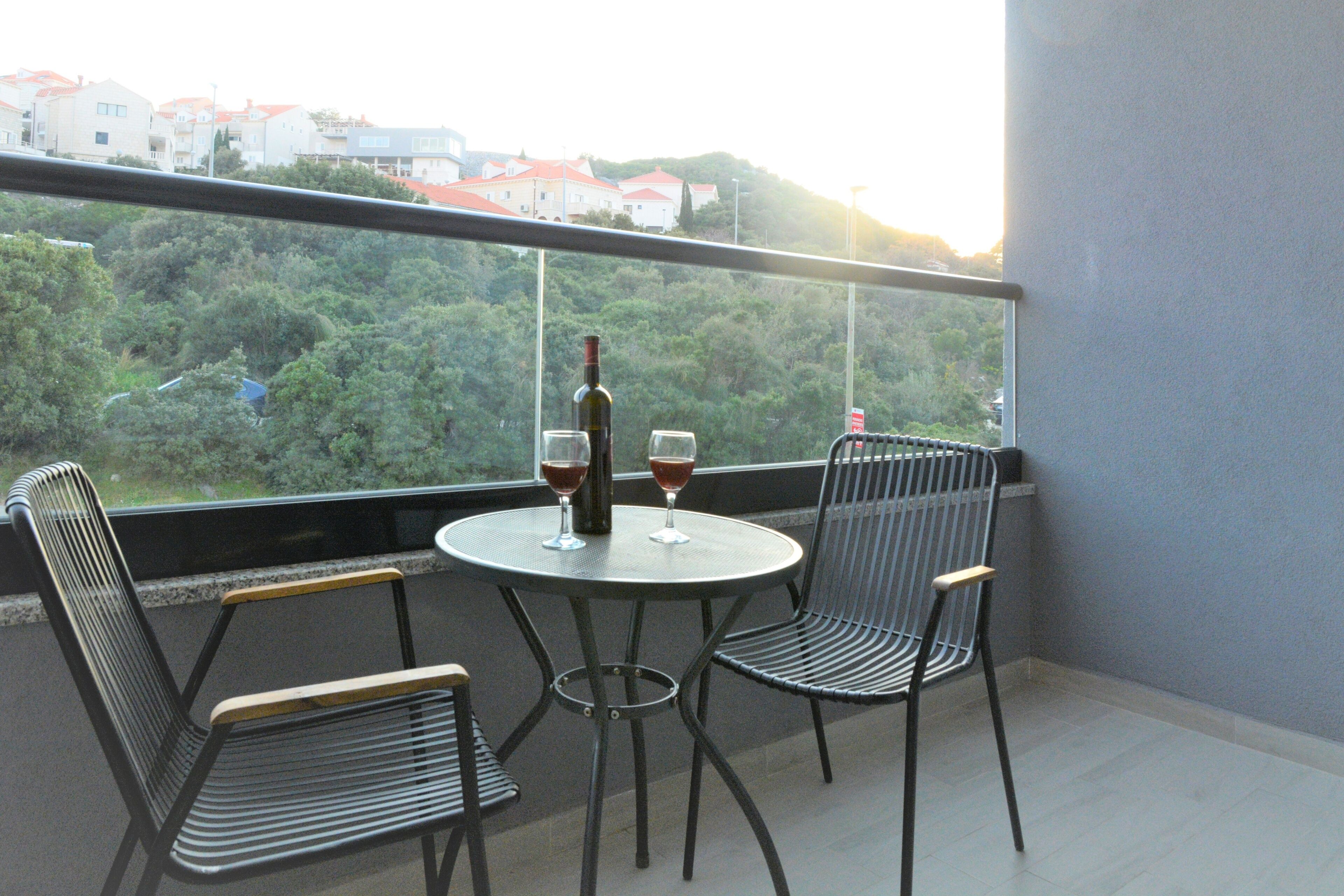 Ein Balkon mit Tisch und zwei Stühlen, einer Weinflasche sowie zwei Weingläsern.