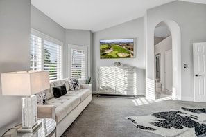 A modern bedroom with a large window, a flat-screen TV, a white dresser, and a patterned rug.