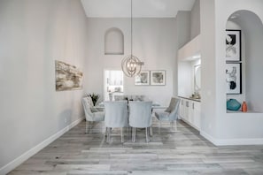 A modern dining area with a herringbone wood floor, white dining chairs, and a central chandelier.