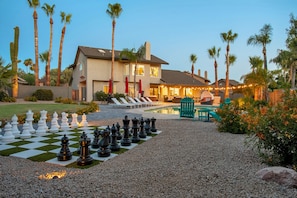 A residential property with a large outdoor chessboard, a swimming pool, and a patio area with lounge chairs and umbrellas.