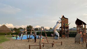 Un parque infantil con diversas estructuras de juego, incluyendo tobogán y columpios, sobre suelo de arena.