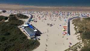 Vista aérea de una playa con numerosos paraguas y gente.