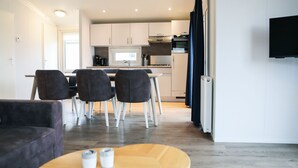 Una cocina moderna con armarios blancos, un comedor con cuatro sillas y un televisor de pantalla plana montado en la pared.