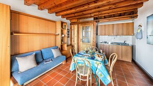 Eine gemütliche Küche mit Holzschnitzschränken, einem Essplatz mit Tellern und Gläsern sowie einem blauen Sofa mit Kissen.