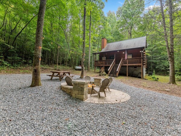 A rustic cabin with a deck, a fire pit, and a picnic table surrounded by chairs. - Lazy Bear Cove - Blue Ridge, GA (Epworth)