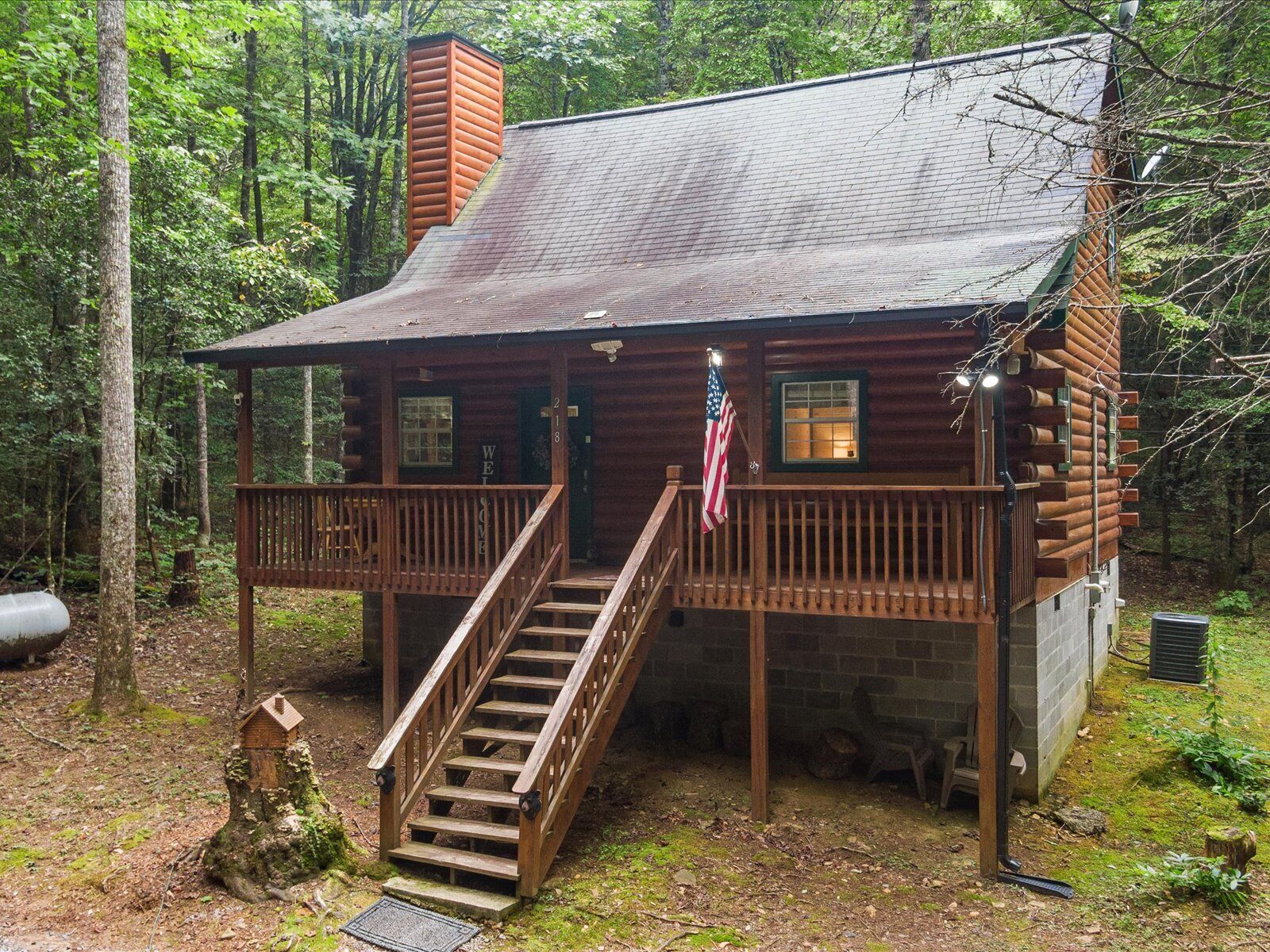 A rustic cabin with a wooden deck, a staircase, and an American flag.