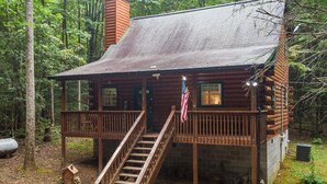 Une cabane rustique dotée d’une terrasse en bois, d’un escalier et d’un drapeau américain.