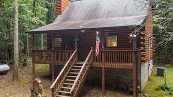A rustic cabin with a wooden deck, a staircase, and an American flag.