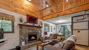 Un intérieur de chalet chaleureux avec une cheminée en pierre, des murs en bois, un canapé confortable et un coin repas.