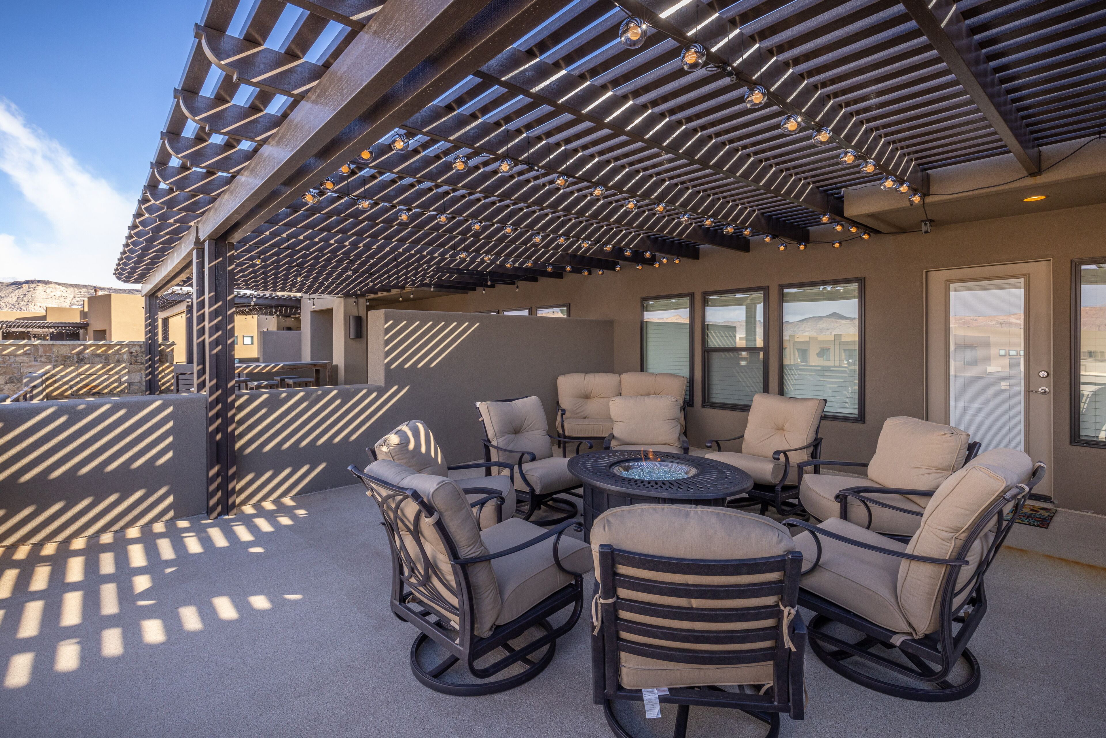 An outdoor patio with a pergola, multiple chairs, and a round table.