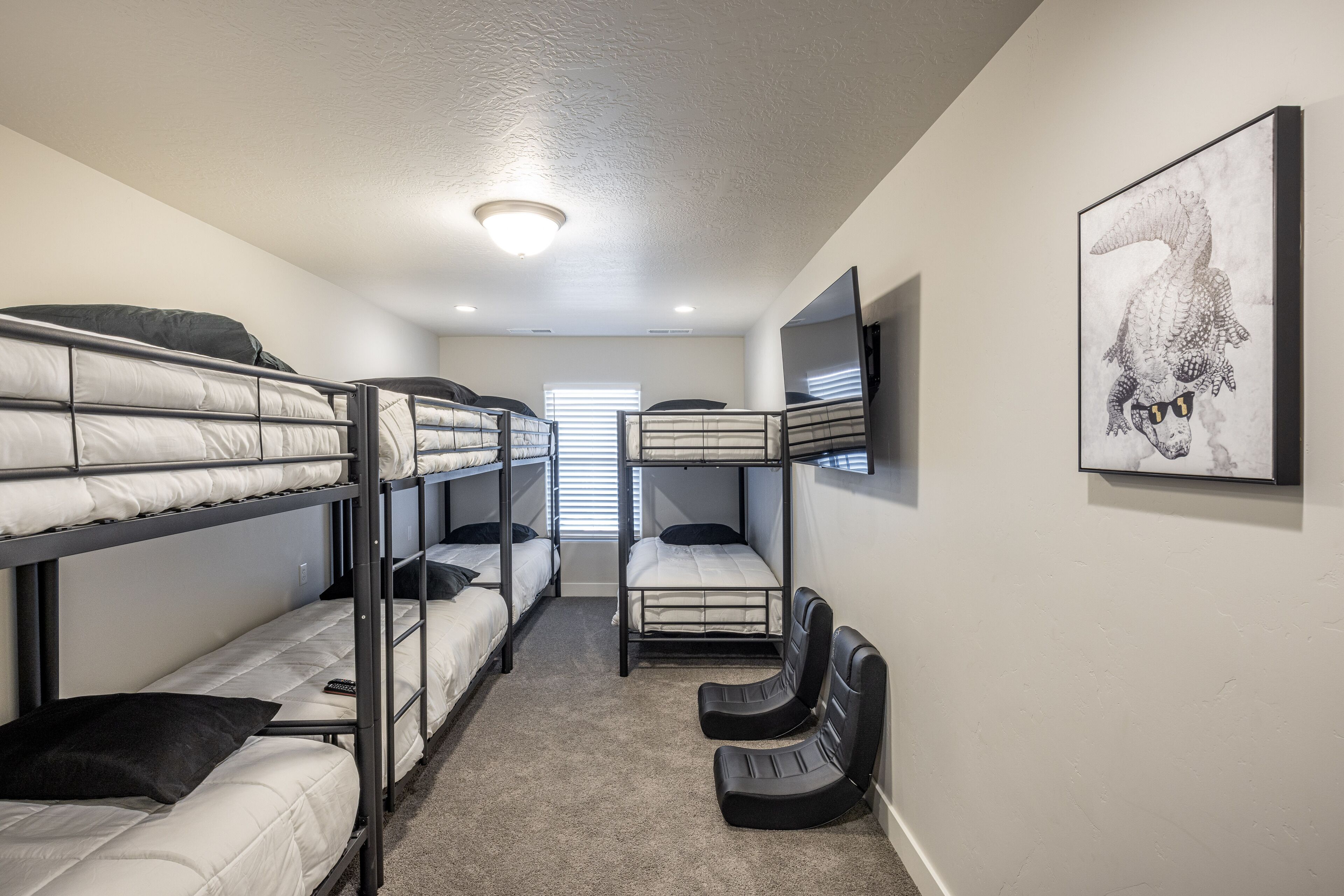A dormitory room with bunk beds, a desk, a chair, and a framed picture on the wall.