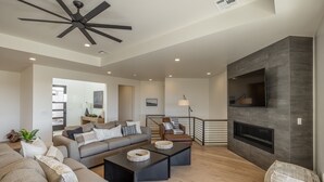 Ein modernes Wohnzimmer mit Kamin, Deckenventilator und einer Treppe zu einer oberen Etage.