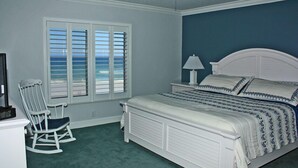 Un dormitorio con cama, una mecedora, una ventana con persianas y un ventilador de techo.