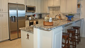 Una cocina moderna con armarios blancos, electrodomésticos de acero inoxidable, encimera de granito e isla integrada con taburetes.