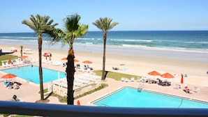 Vista de una playa con piscina, palmeras y sillas de playa.