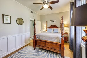 A four-poster bed with a wooden frame and a light-colored bedspread, a ceiling fan, and a wall-mounted light fixture. - Pet-Friendly Home w/ Fenced Yard in Texarkana (Texarkana)