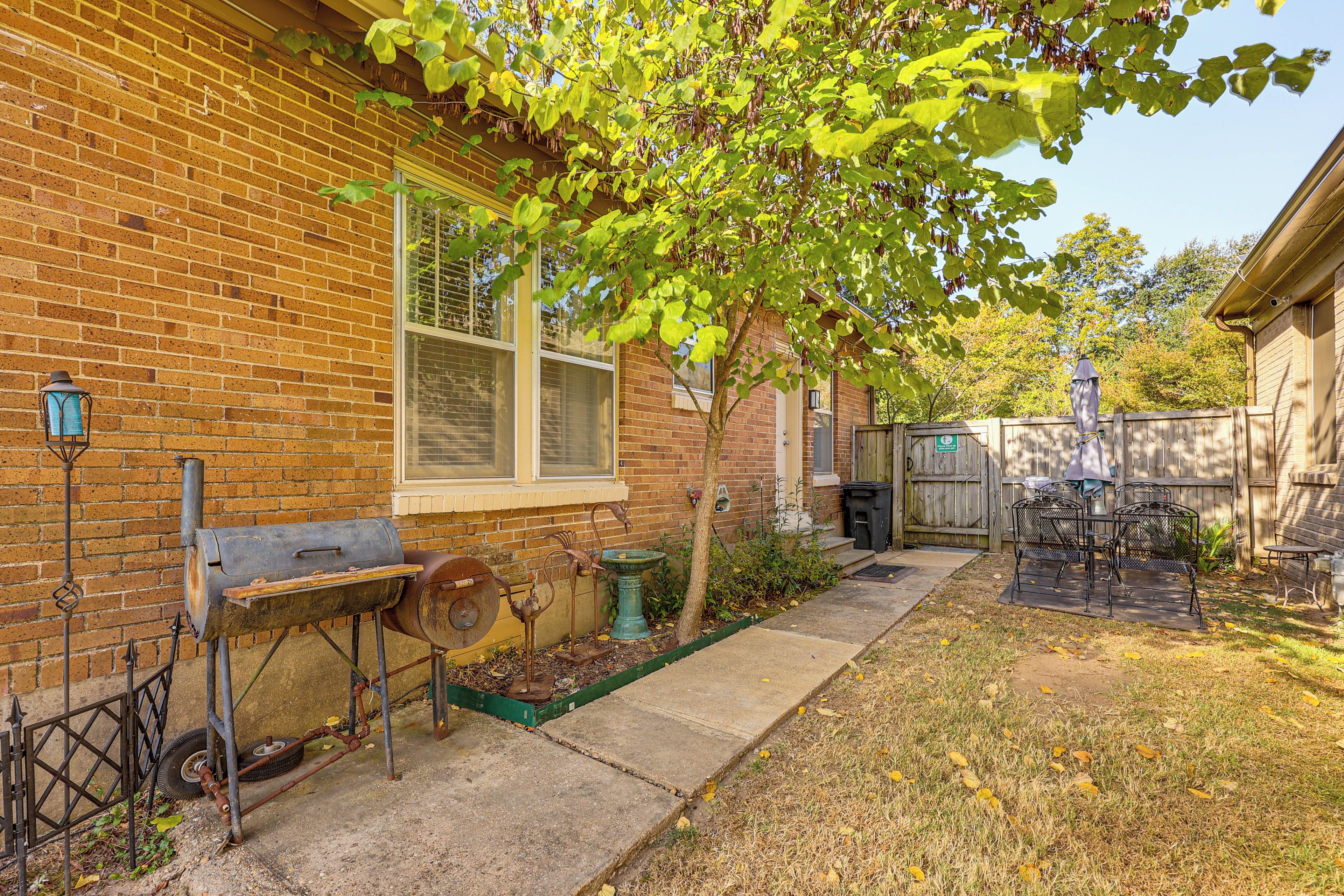 A brick house with a window, a metal grill, a tree, and a wooden fence.