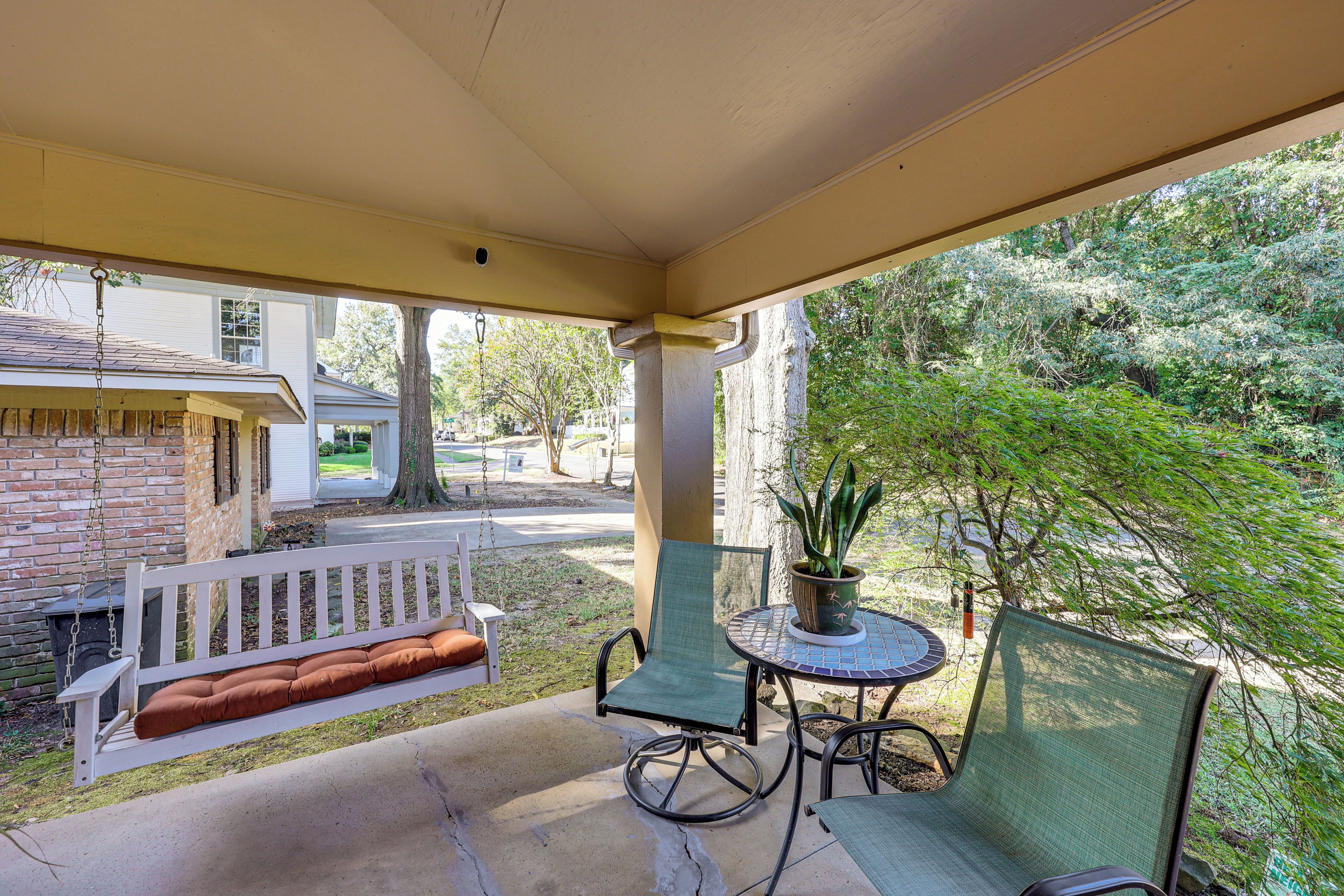 A covered porch with a swing, a table with chairs, and a potted plant.