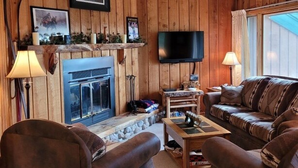 Un salon chaleureux avec une cheminée, des murs en bois, un téléviseur et des sièges confortables.