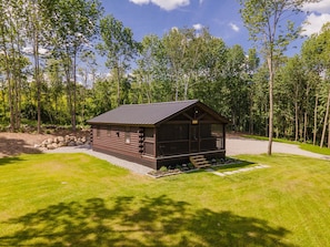 Situated in a lush environment, this cabin features a front porch and a well-maintained lawn.
