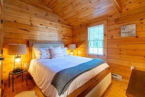 Cozy cabin-style accommodation with a large bed, bedside table, and window with blinds.