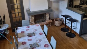 Ein Essbereich mit Tisch für vier Personen, einem Kamin, einer Küchenzeile mit Fernseher und einer Tür mit satinierten Glasscheiben.