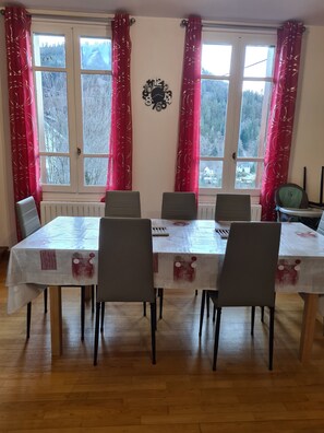 A dining area with a table set for four, surrounded by chairs, and a view of a snowy landscape through large windows with red curtains.