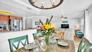 A modern kitchen with stainless steel appliances, a dining area with a wooden table and chairs, and a living room with a sofa and TV.