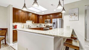 A modern kitchen with wooden cabinets, a granite countertop, and stainless steel appliances. - 137 Beachwalk Villa Steps To The Beach (Hilton Head Island)