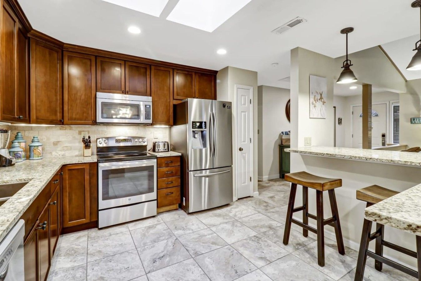 A modern kitchen with wooden cabinets, stainless steel appliances, a marble countertop, and a skylight.