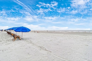 Una playa con hileras de sombrillas azules y sillas.