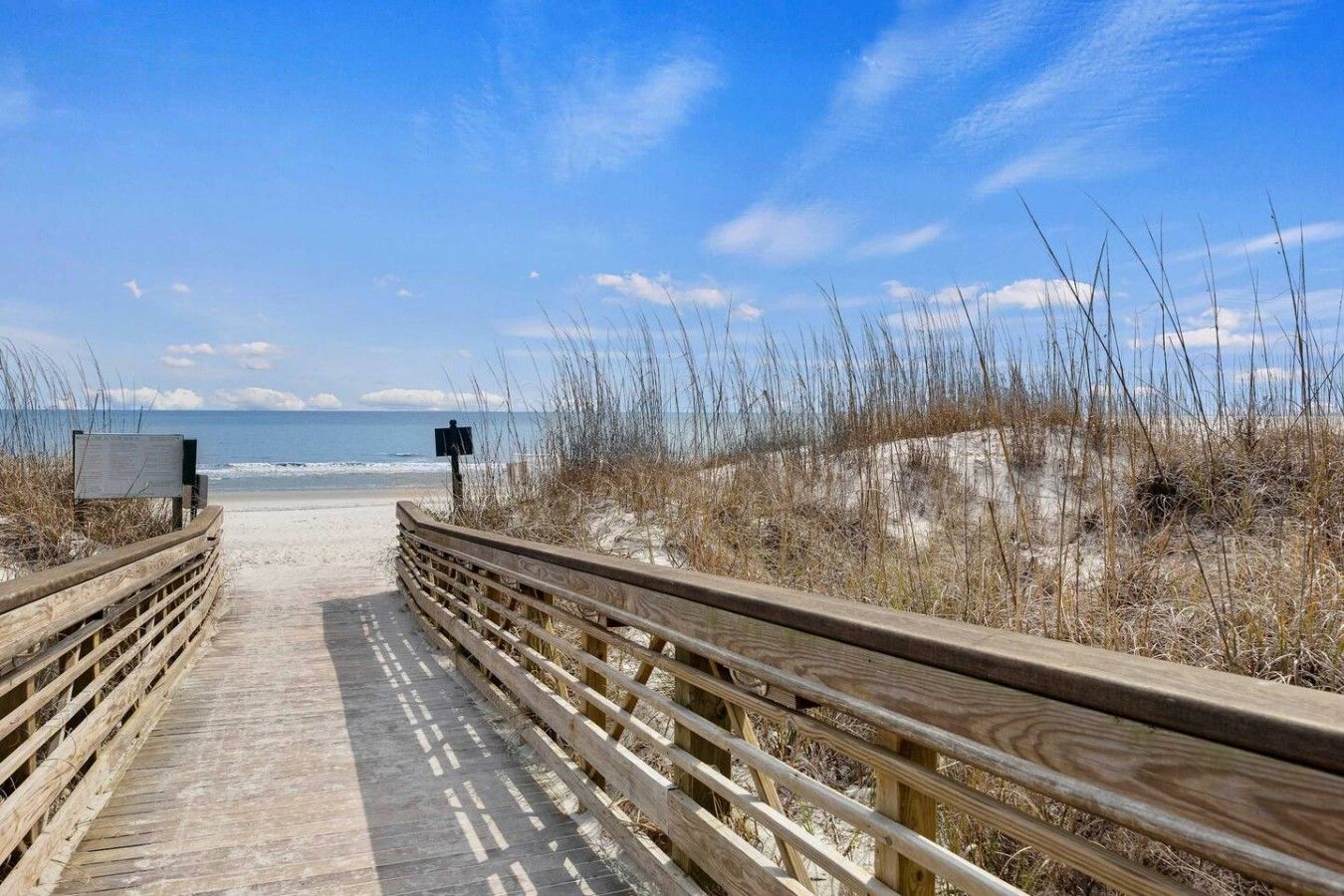 A wooden boardwalk leading to a beach with a clear sky.