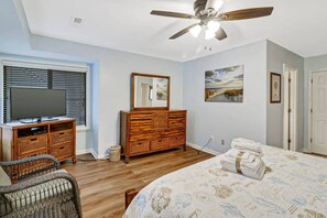 Un dormitorio con cama, cómoda, televisor, ventilador de techo y un cuadro en la pared.