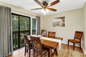 Un comedor con una mesa, sillas, un ventilador de techo y un amplio ventanal con cortinas.