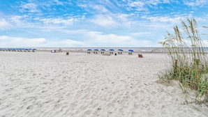 A beach with rows of blue umbrellas and beach chairs, a tent, and sparse vegetation. - 137 Beachwalk Villa Steps To The Beach (Hilton Head Island)