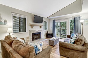 Un salon avec une cheminée, un téléviseur et un balcon donnant sur l’extérieur.