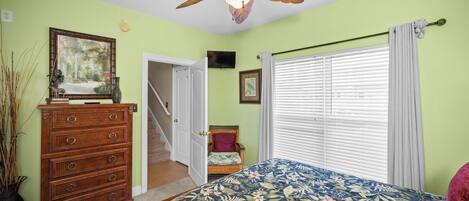 A bedroom with a bed, dresser, ceiling fan, and a staircase leading to another room.
