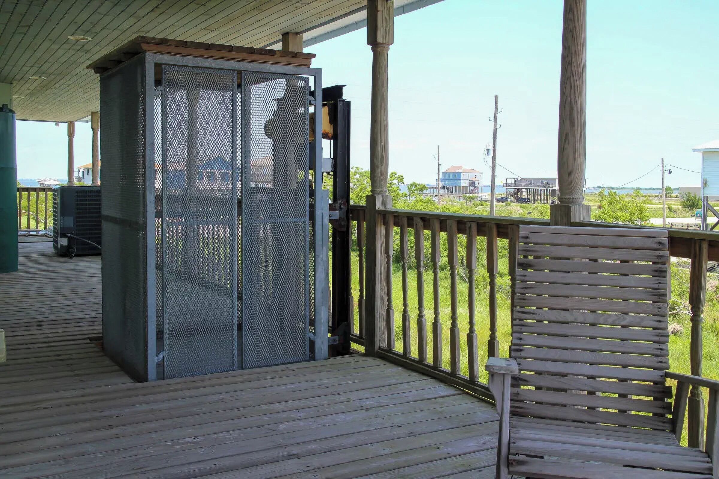 A covered outdoor area with a wooden deck, a metal grill enclosure, and a wooden chair.