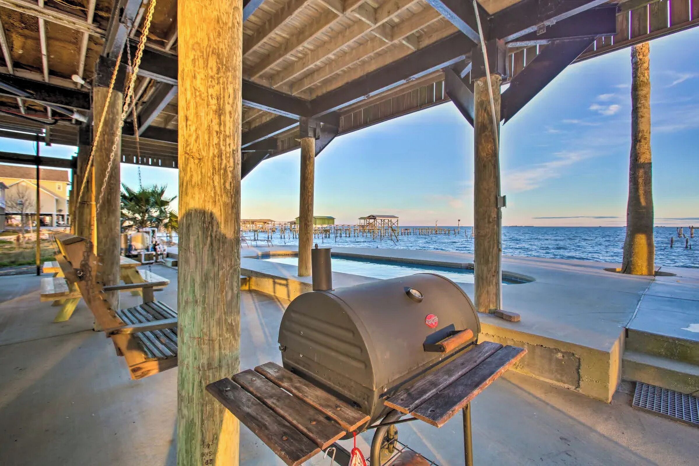 A covered outdoor area with a barbecue grill, wooden benches, and a view of the beach and ocean.