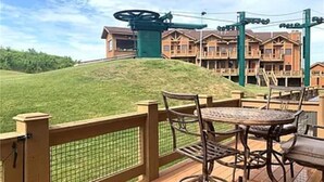 Une terrasse dotée de mobilier d’extérieur et offrant une vue sur un immeuble à multiples fenêtres, avec une structure verdoyante en arrière-plan.