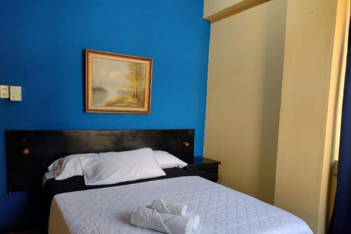 Une chambre d’hôtel avec un lit, un tableau au mur et une fenêtre avec des rideaux.