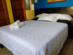 Un lit bien fait, recouvert d’une courtepointe blanche matelassée, avec des serviettes blanches pliées enroulées sur le côté.