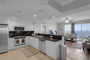 A modern kitchen with white cabinetry, a central island, and a view to the living area.