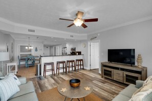 A modern living room with a sofa, a coffee table, a TV, and a kitchen area in the background.