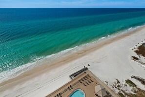 An aerial view of a beach resort with a swimming pool, sun loungers, and a clear view of the ocean.