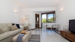 A modern living room with a sofa, coffee table, TV, dining area, and large windows. - Apartment Salgados Lounge - By D´alma Portuguesa (Albufeira)