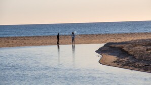 A beach with two people standing on the sand, a calm sea, and a clear sky. - Apartment Salgados Lounge - By D´alma Portuguesa (Albufeira)
